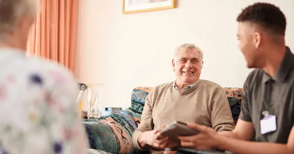 Smiling senior man sitting with a healthcare worker during a home visit, discussing care options provided through Medicaid MCO.