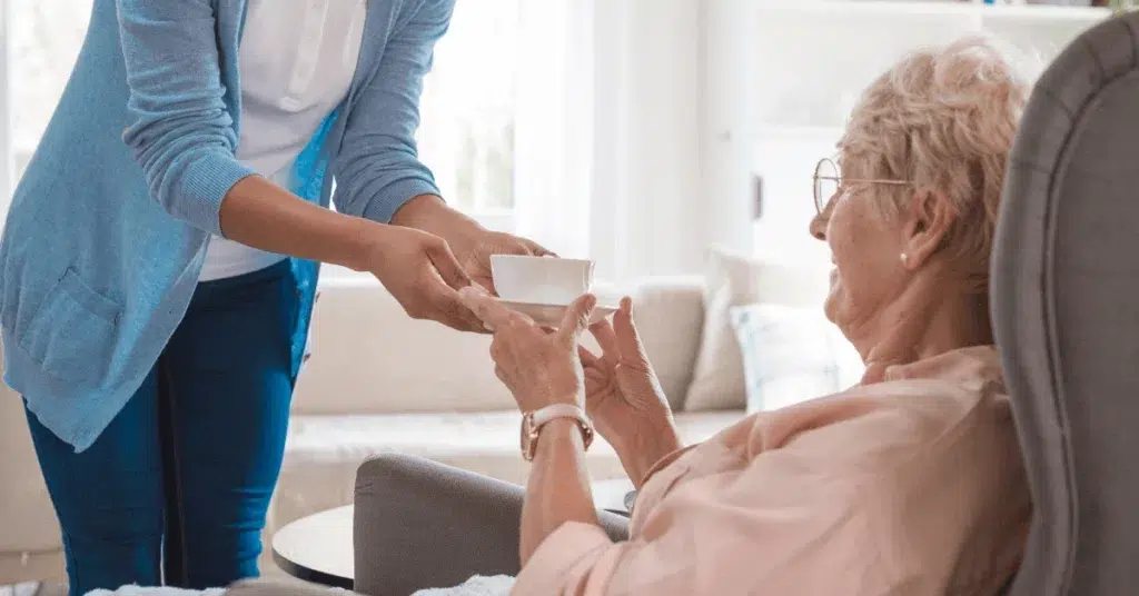 Caregiver handing a cup of tea to an elderly woman at home, representing support services available through Pennsylvania Medicaid.